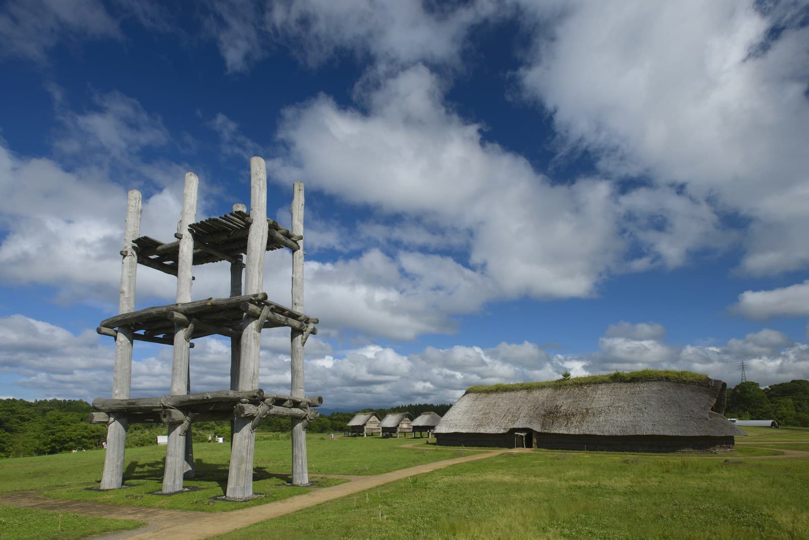 A reconstructed six-pillar wooden tower and a large thatched pit dwelling on grass