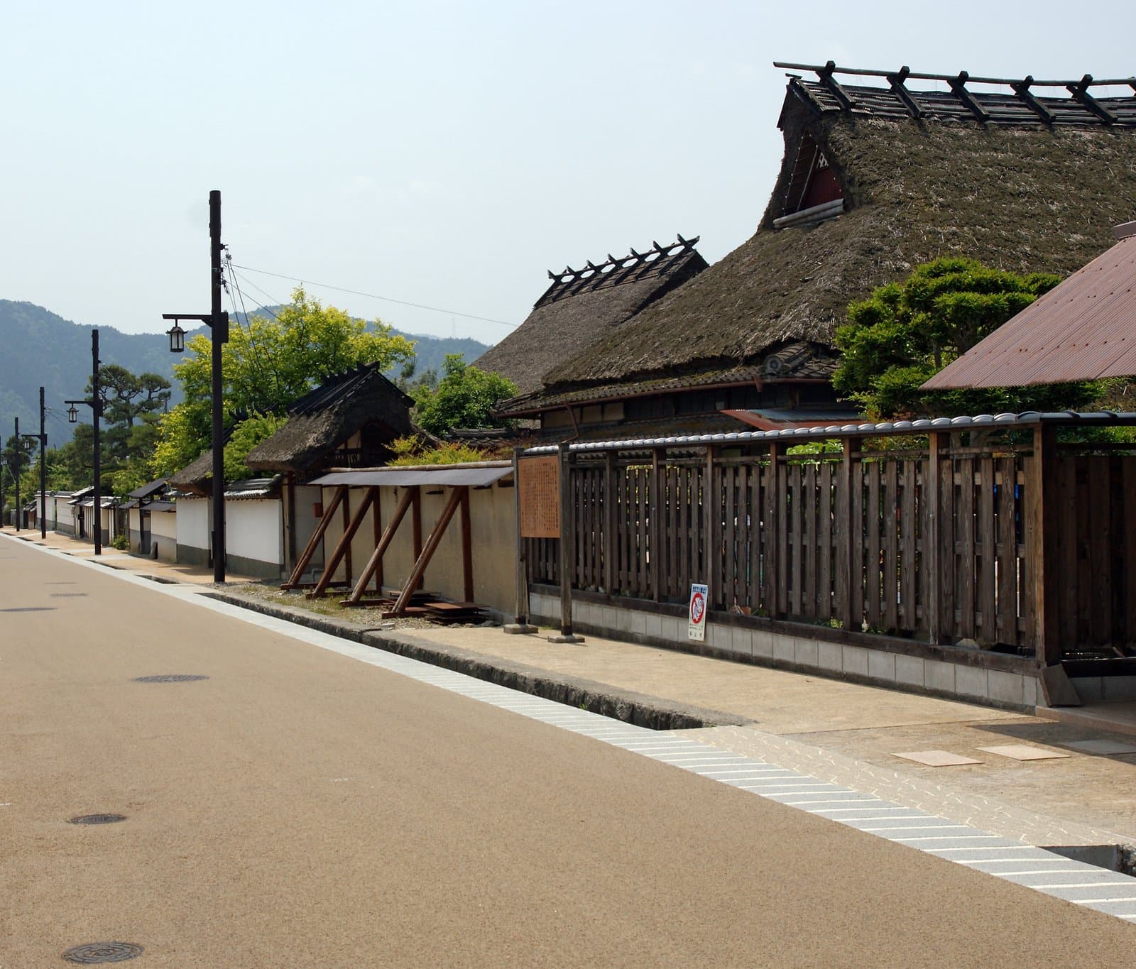 A quiet street of old houses with thatched roofs and white walls, with green hills beyond