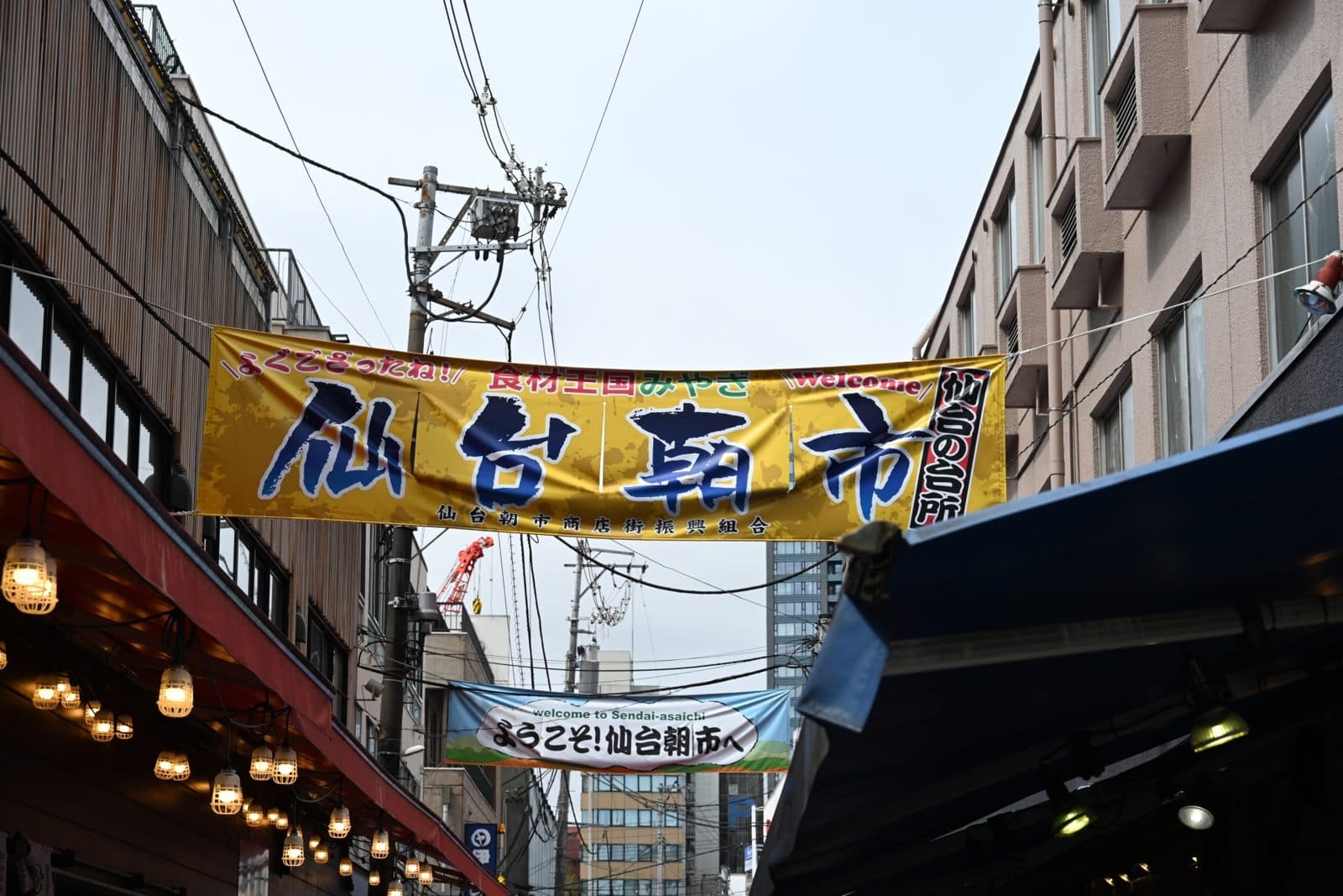 A shopping street with a large "Sendai Asaichi" banner hung between buildings
