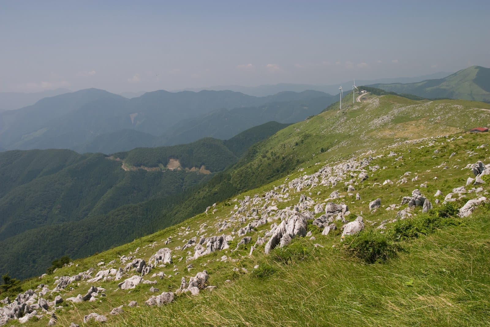 A grassy ridge dotted with white limestone rocks, with mountain ranges beyond