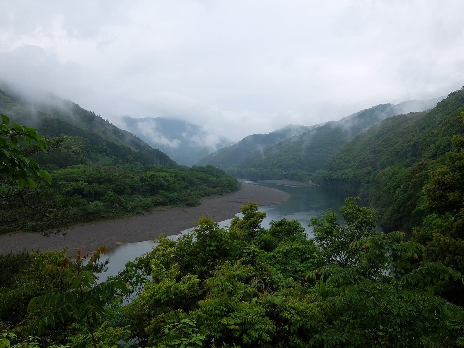 A wide river winding between green mountains under misty clouds