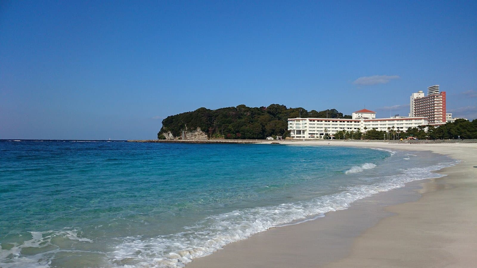 A white sand beach curving along turquoise water, with hotels on a green point