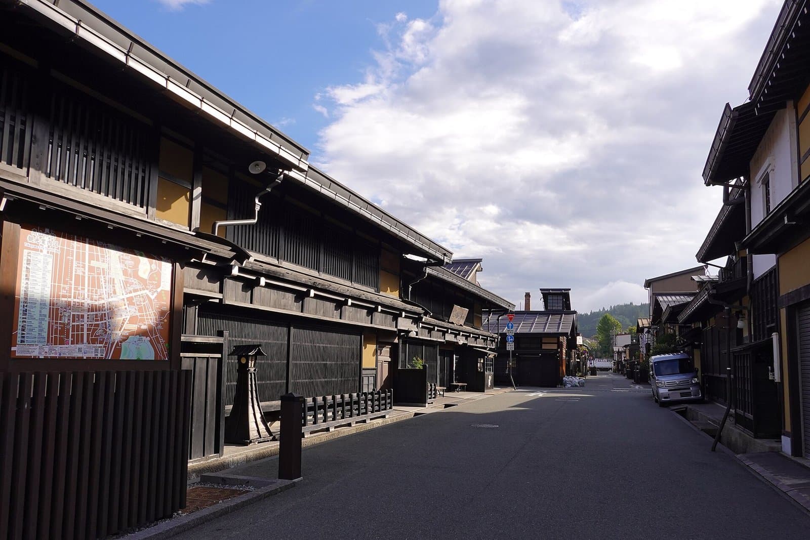 A quiet street lined with dark wooden latticed merchant houses under a blue sky with clouds