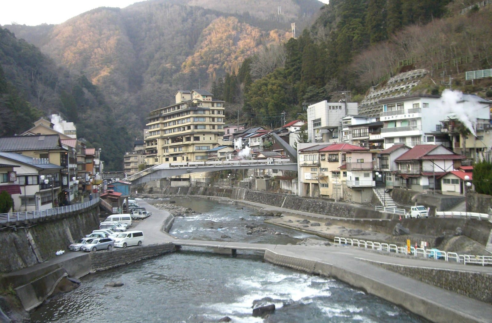 険しい谷の岩の多い川沿いに旅館が並び、湯けむりが上がる温泉街