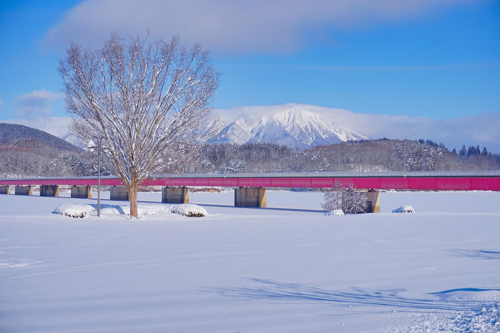 A red bridge across a frozen, snow-covered lake, with snowy Mt. Iwate behind