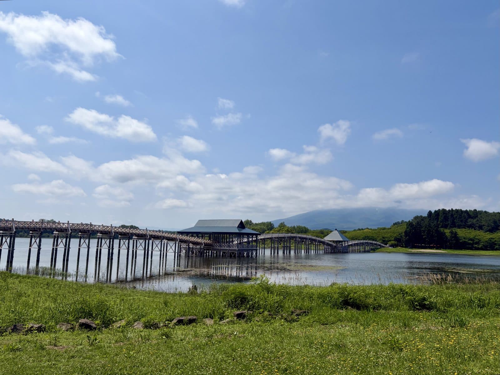 The long wooden Tsuru-no-Mai Bridge across a lake, with Mt Iwaki behind and a grassy bank in front