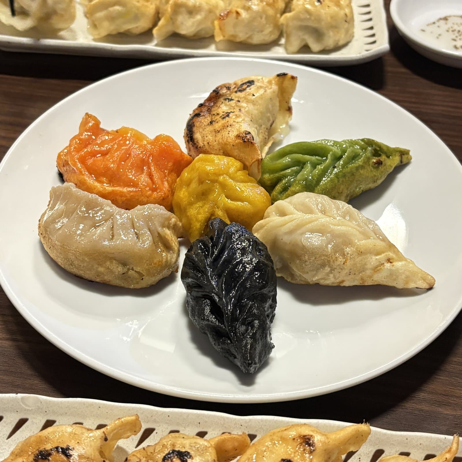 白い皿に円く並んだ色とりどりの焼き餃子と、細長い皿の餃子