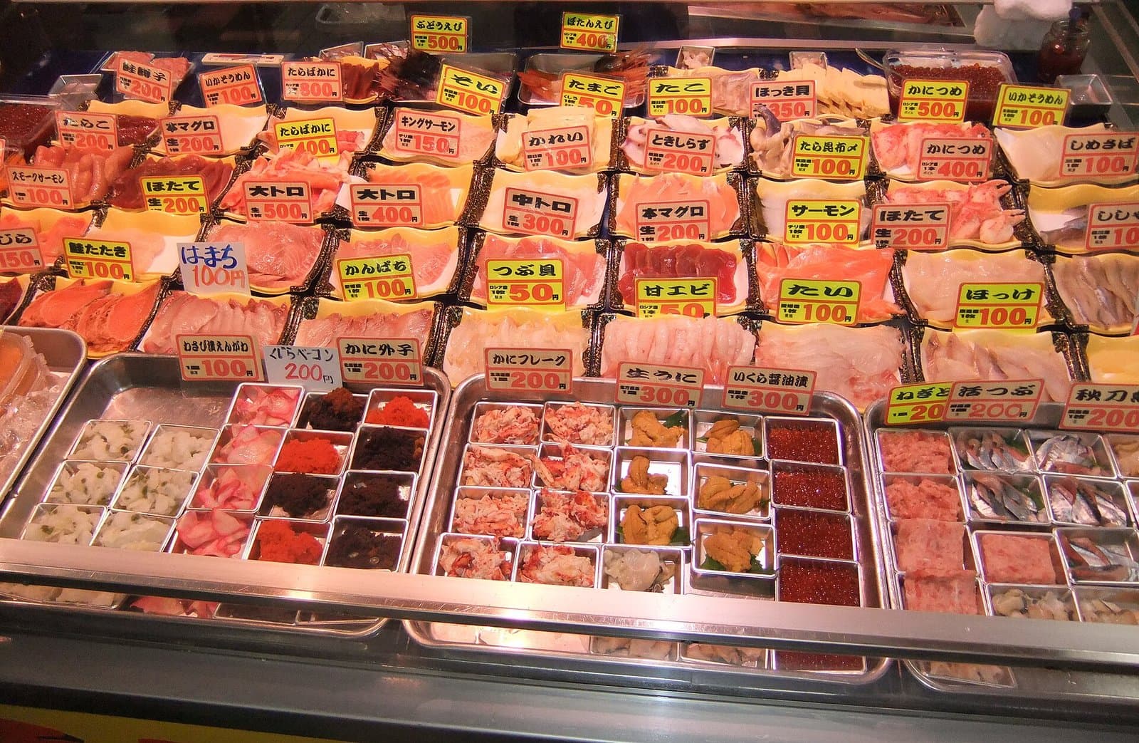 Trays of sliced seafood toppings with price tags at a market stall