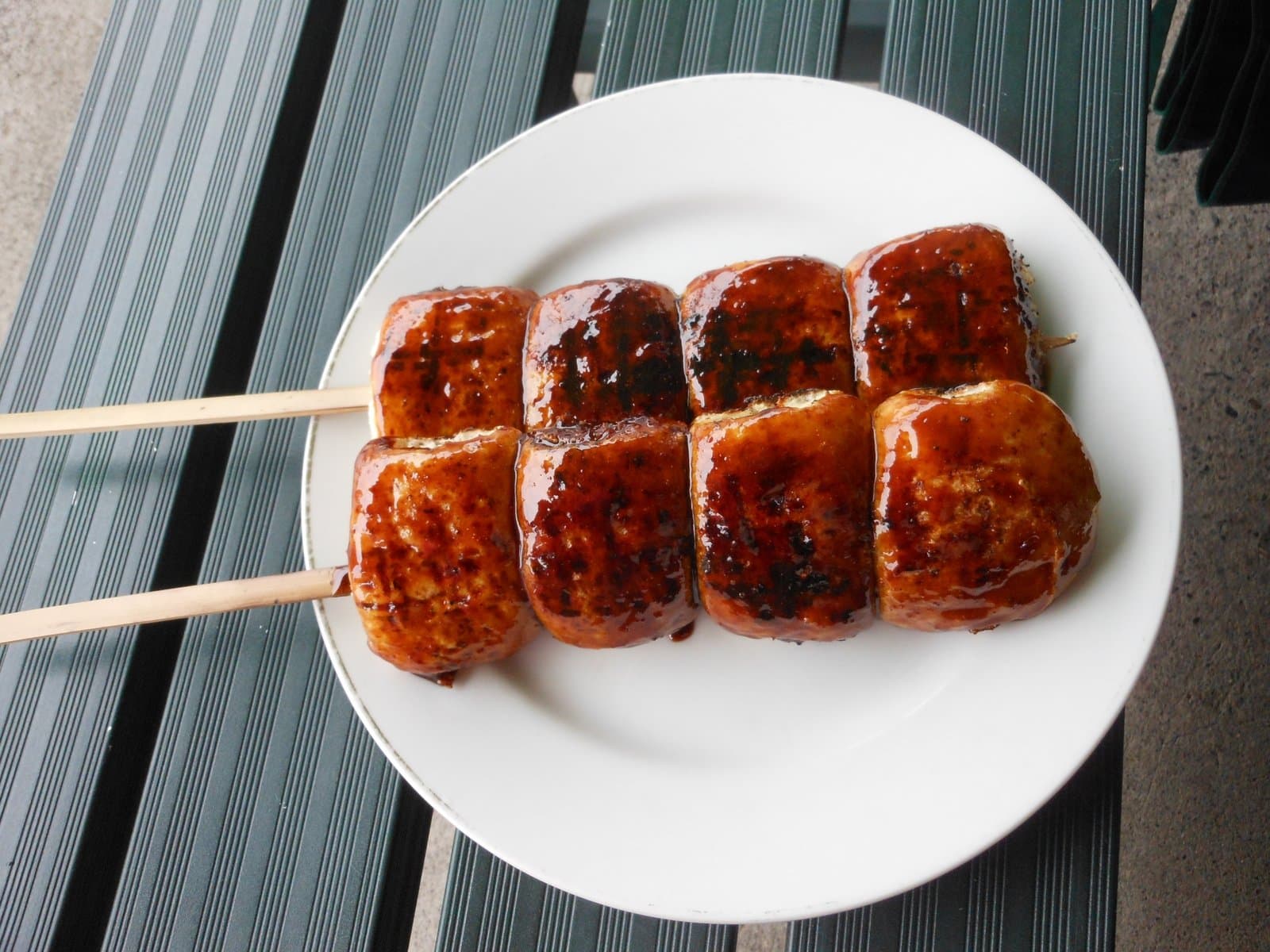Two skewers of grilled buns glazed with a dark sweet miso sauce on a white plate