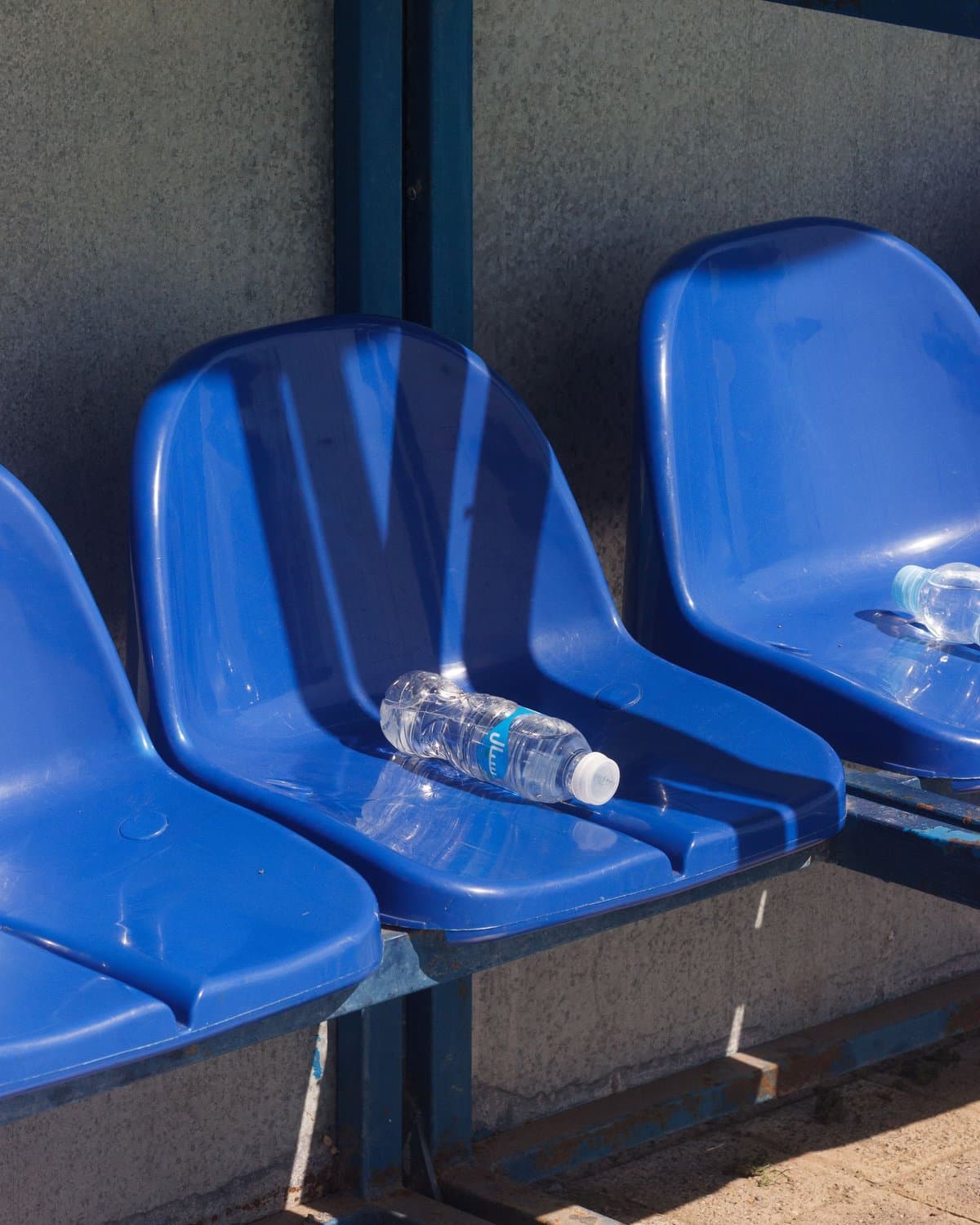 A water bottle on blue stadium seats in the sun