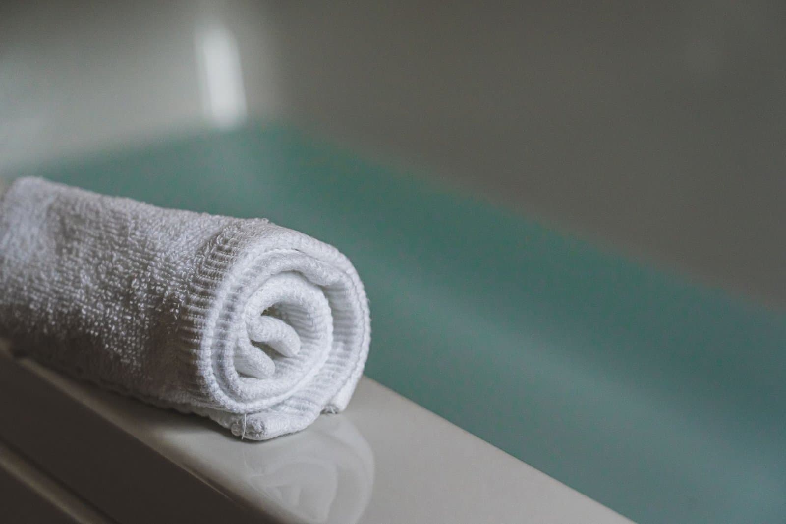A rolled white towel on the edge of a bath