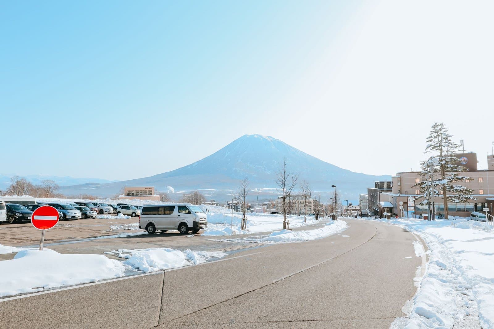 A snowy road and parking area with a snow-capped mountain beyond