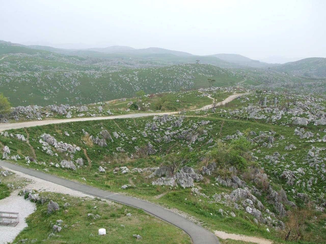 A grassy plateau scattered with white limestone rocks, crossed by paved paths