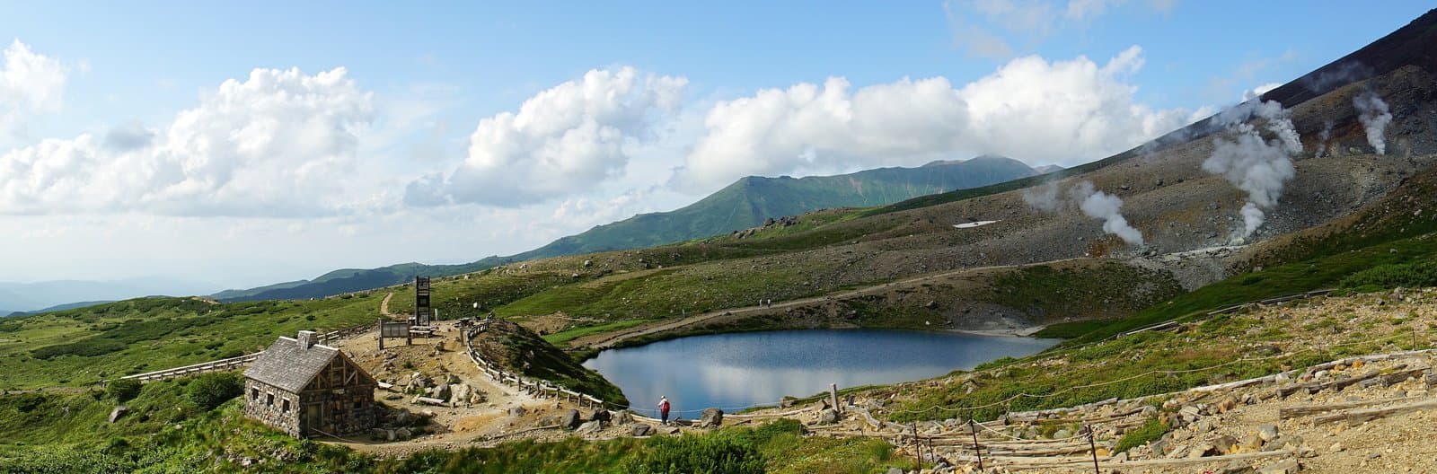 Sugatami Pond below the steaming slopes of Mt Asahidake, with a stone hut and walking trails