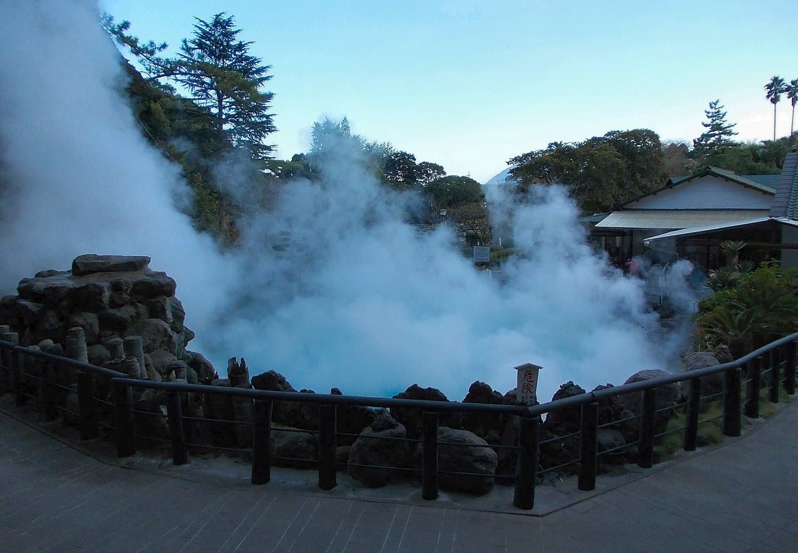 低い柵の向こうで、温泉の池から立ちのぼる白い湯けむり