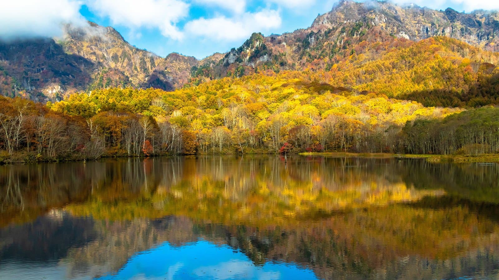 Rugged mountains and yellow autumn trees reflected in a still pond