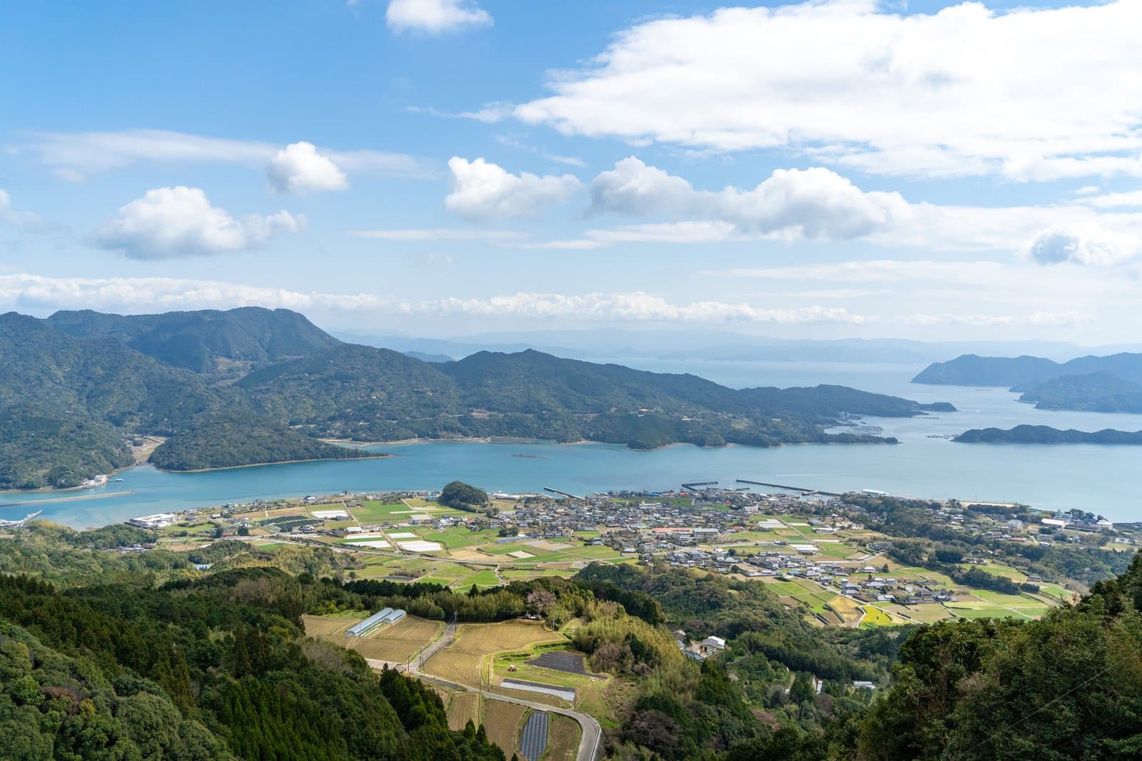 山頂から見渡す、緑の丘と湾、田畑、沖の島々