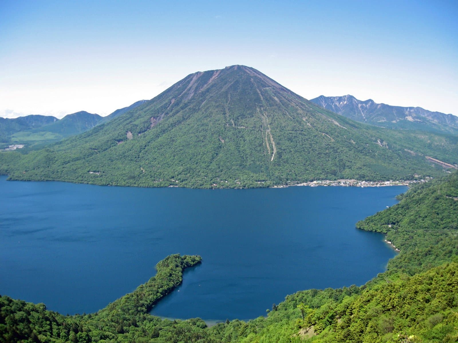 A deep blue lake below a cone-shaped green mountain, seen from a hillside