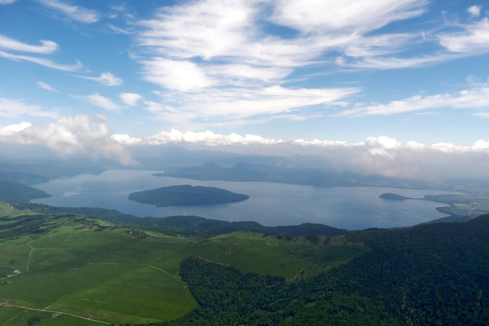 Lake Kussharo with Nakajima island, seen from high green grassland under a blue sky