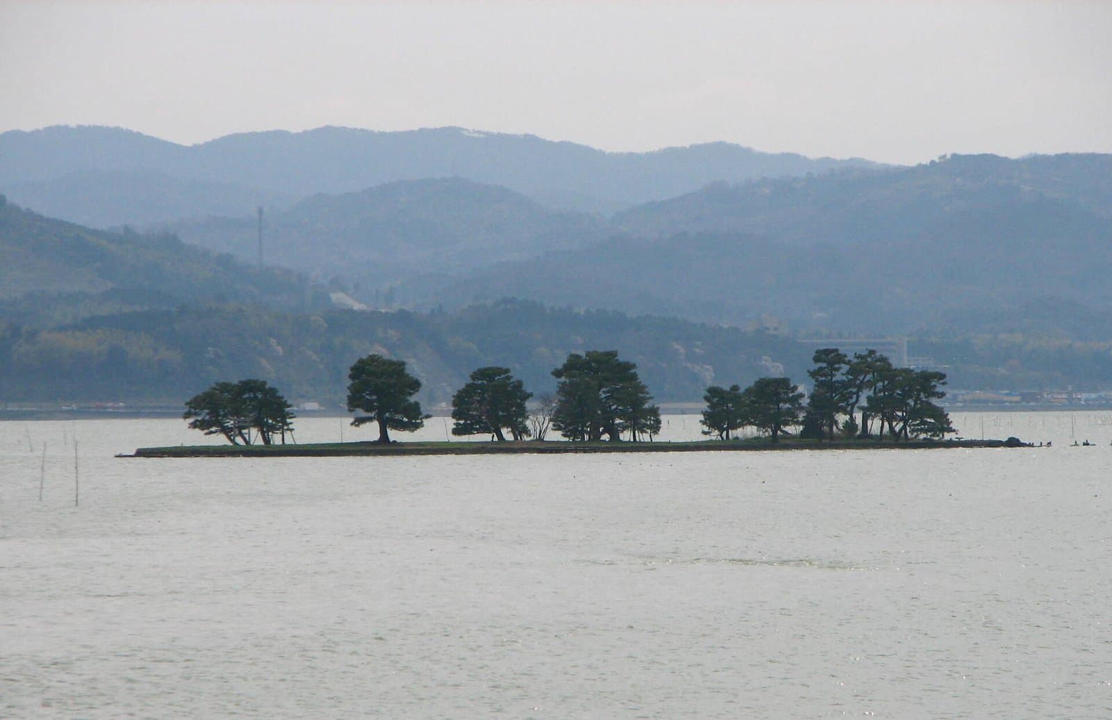 静かな湖に浮かぶ松の並んだ小島と、奥のかすんだ山々