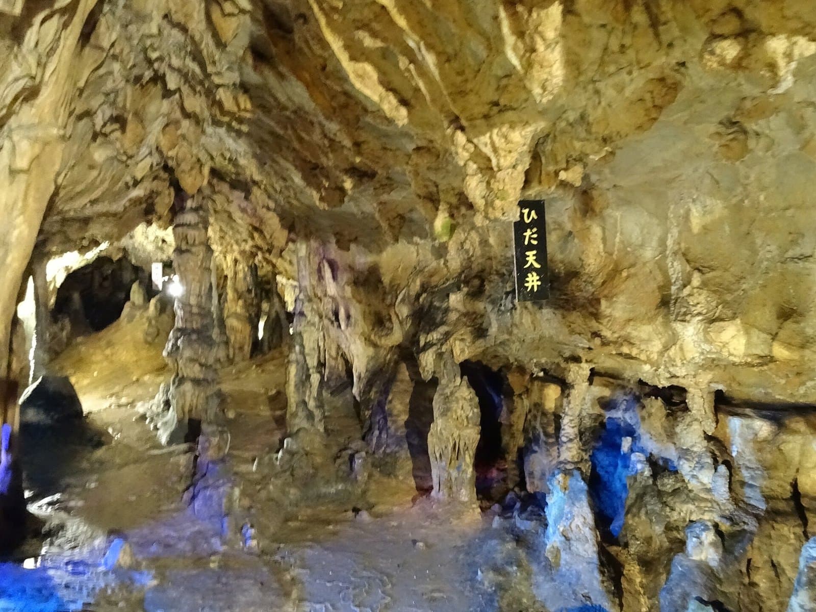 The folded rock ceiling and walls of a limestone cave, lit in yellow and blue