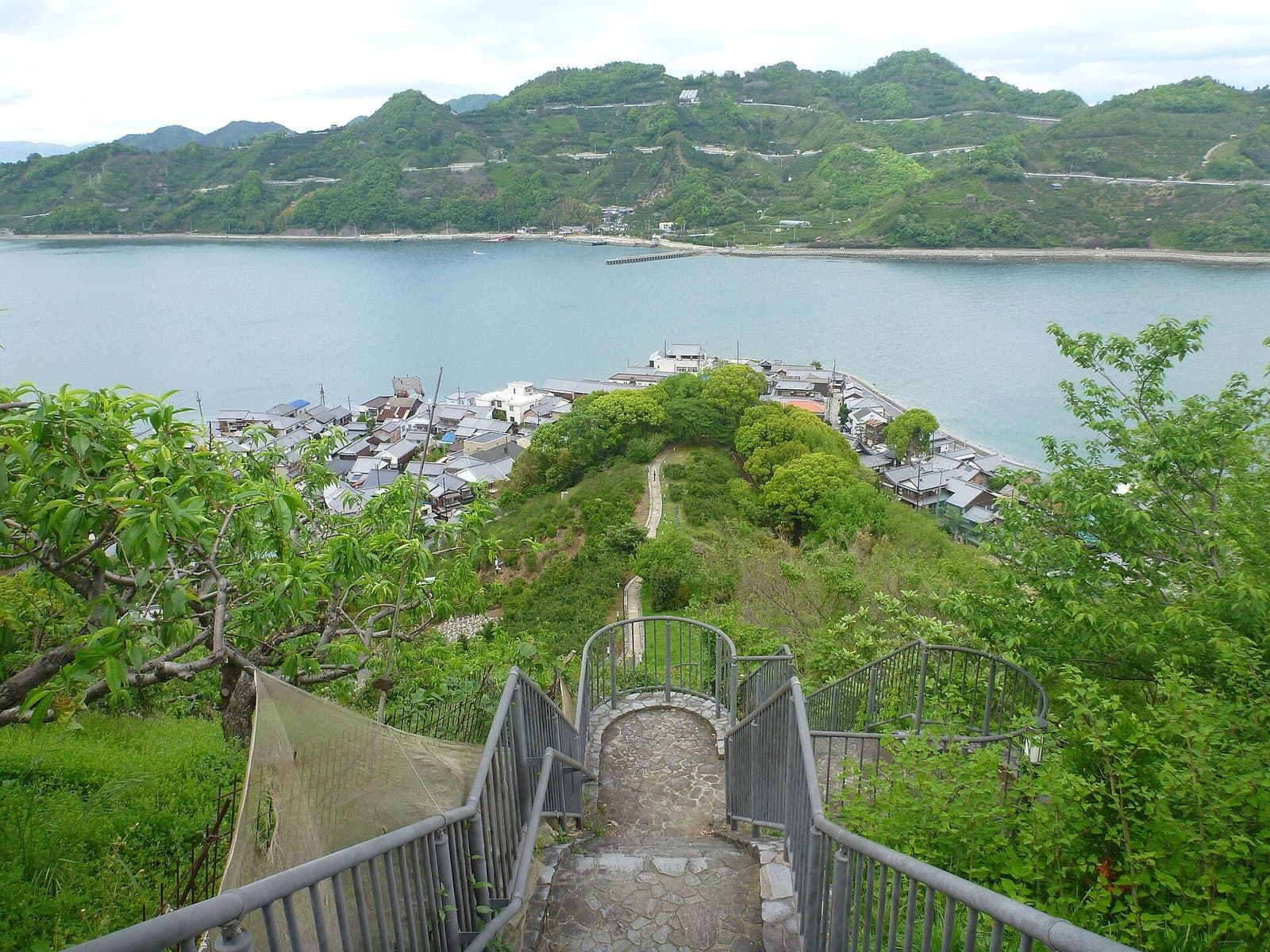 Rooftops of Mitarai along the shore seen from a hillside path, with the sea and green hills beyond