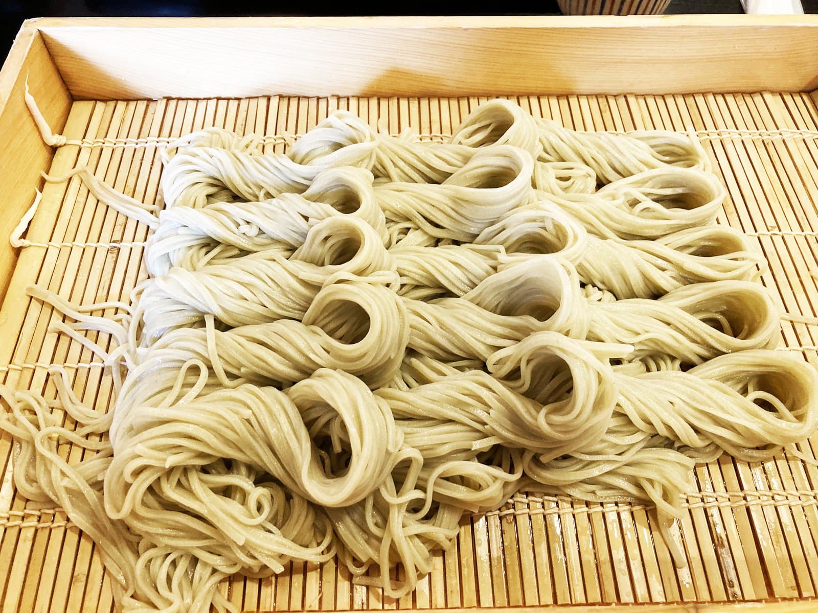 Soba laid out in neat loops on a bamboo mat in a wooden tray