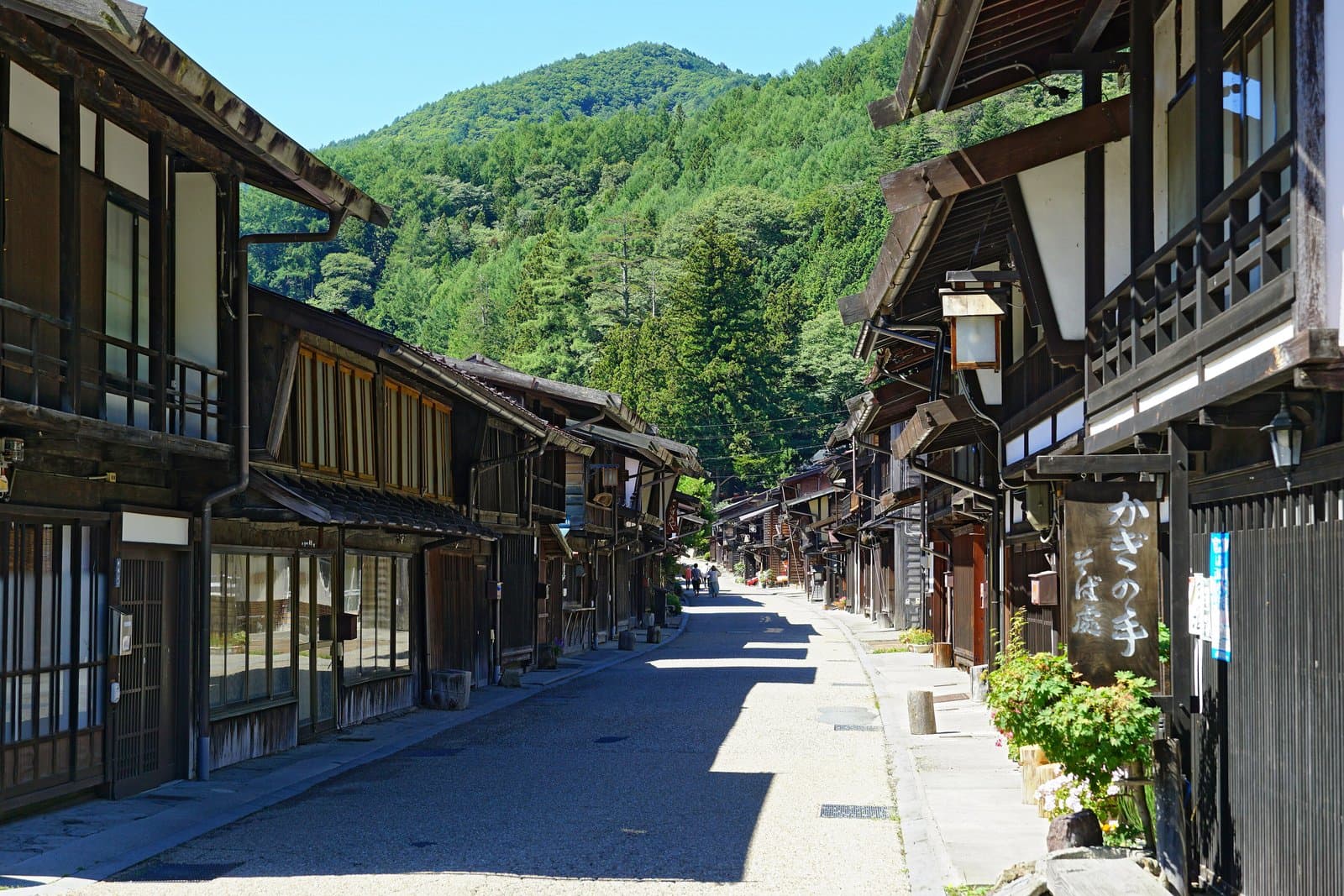 A long straight street lined with dark wooden two-storey houses below green mountains