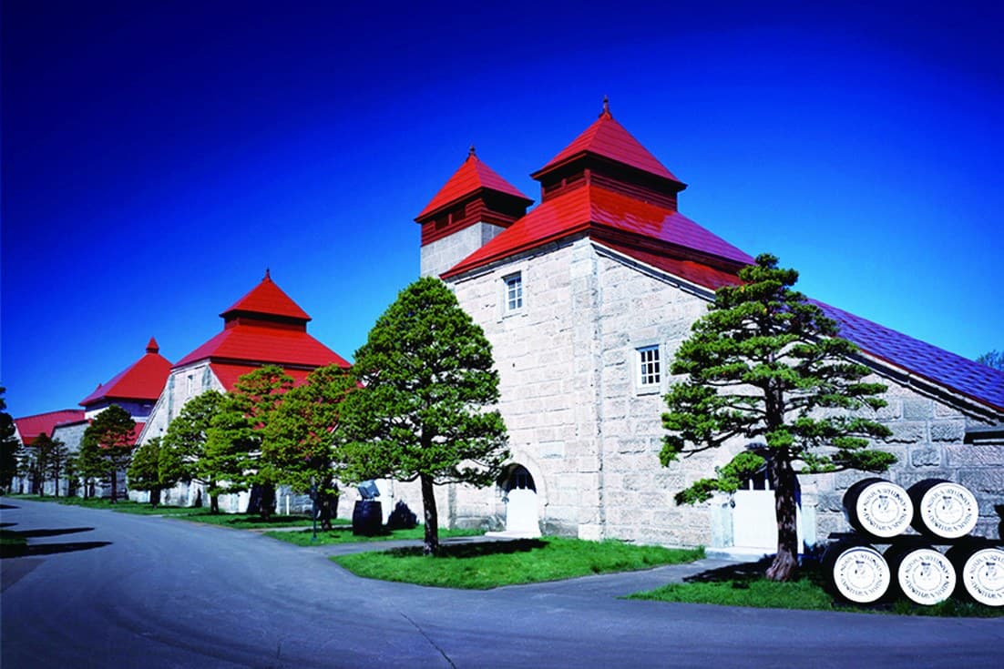 Stone distillery buildings with red pagoda roofs, pine trees and whisky barrels