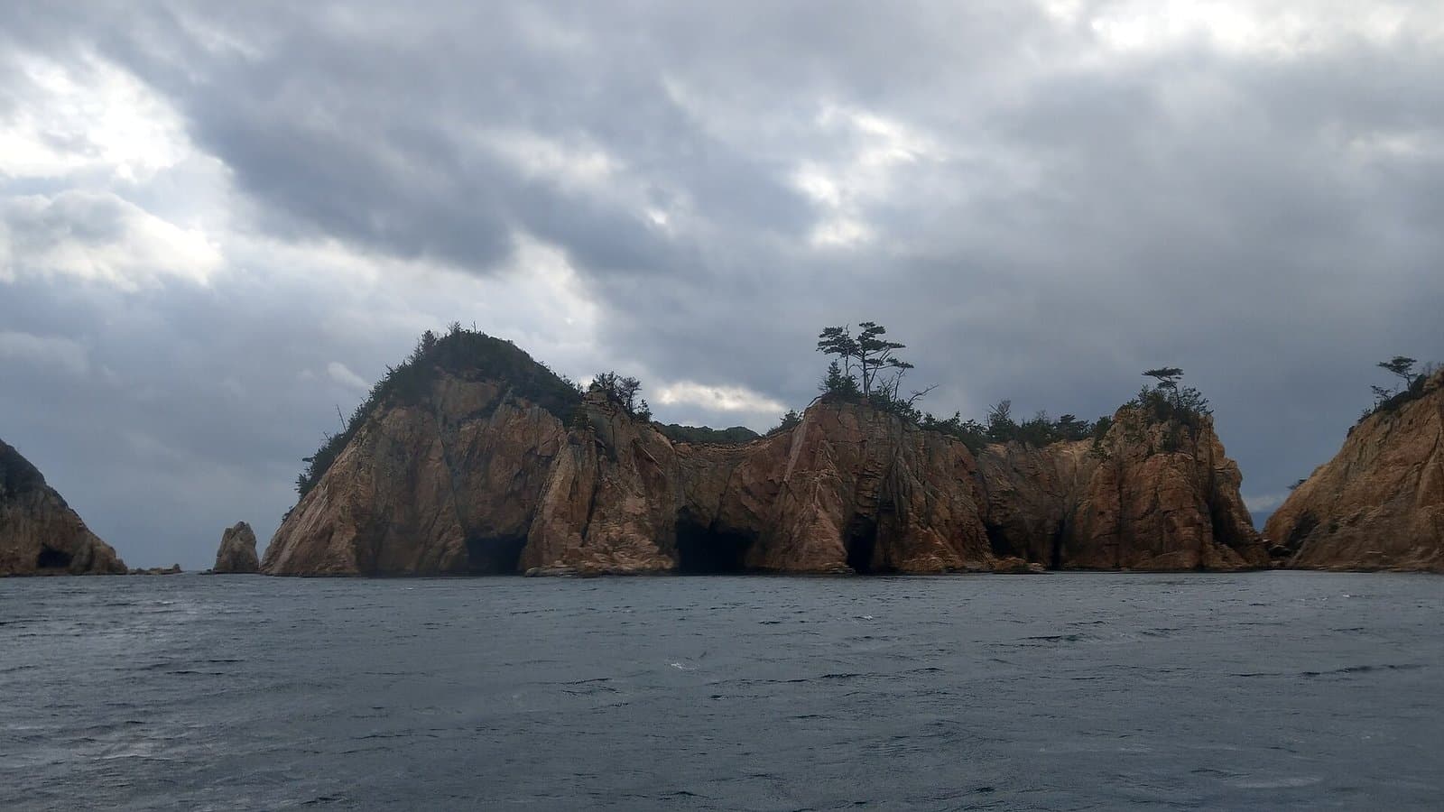 A rugged island of steep rocky cliffs and caves, seen from the sea