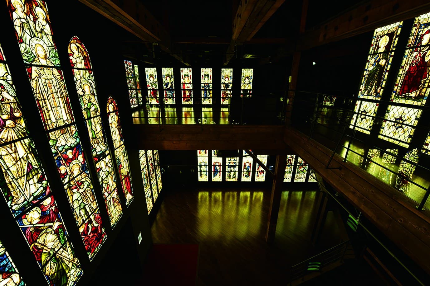 A dark hall lined with tall lit stained-glass windows