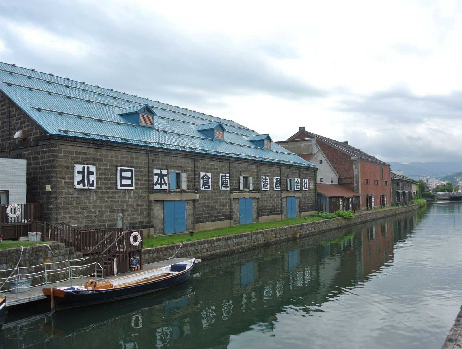 Stone warehouses with a blue roof along Otaru Canal, with a wooden boat moored in front