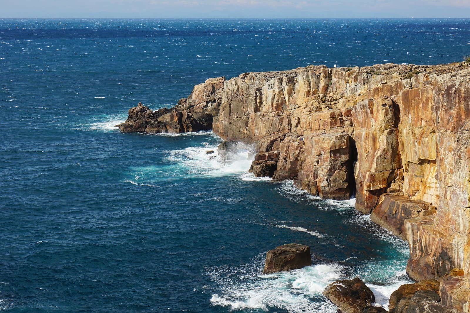 Sheer layered cliffs dropping into a deep blue sea with white waves
