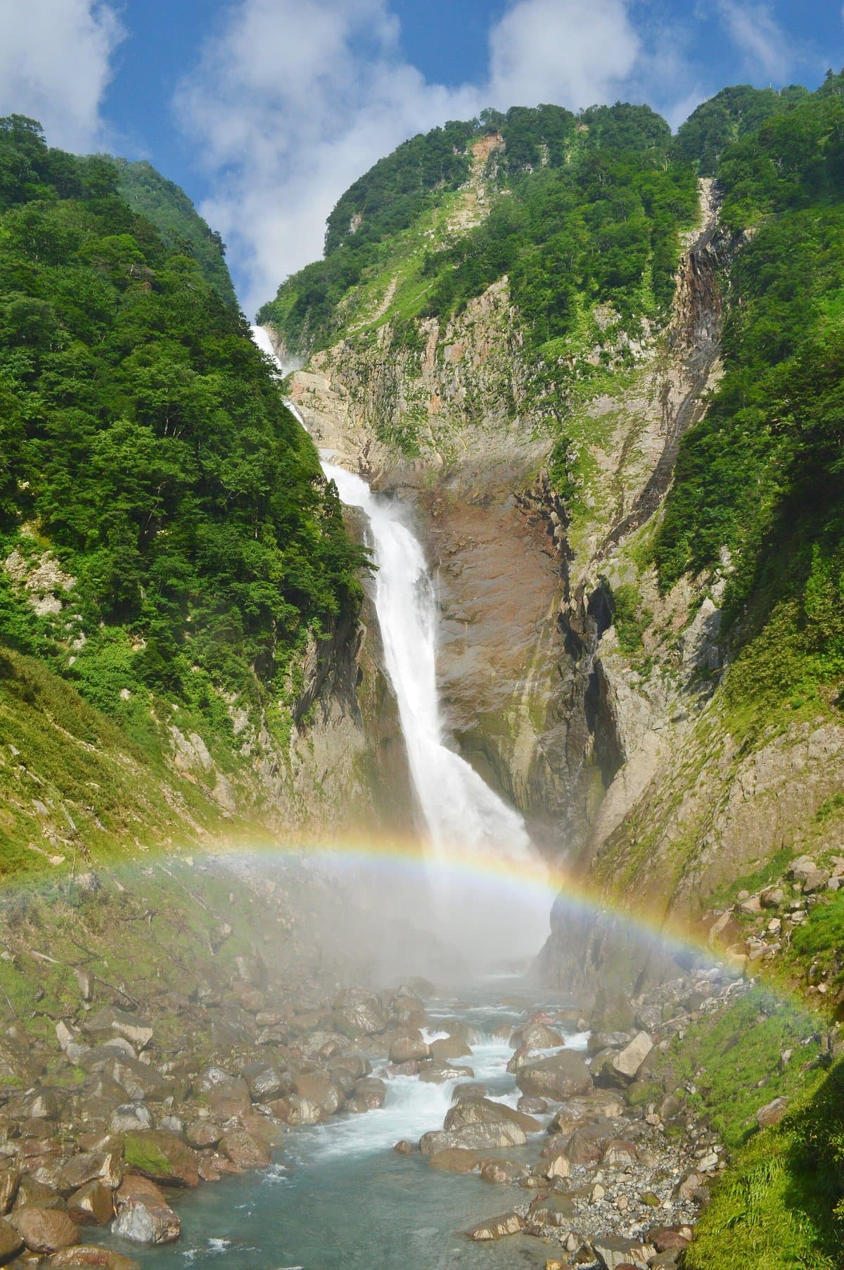 緑の谷を落ちる高い滝と、水しぶきにかかる虹