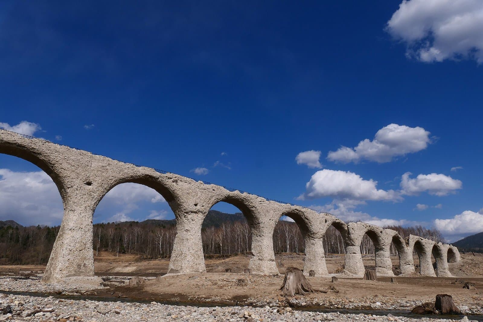 A long row of weathered concrete arches standing on the dry lakebed under a deep blue sky