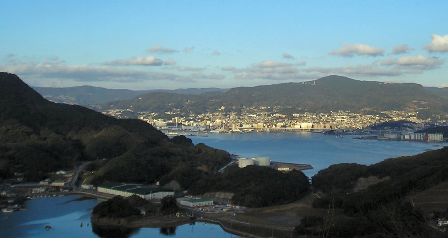 An inlet with wooded islands and a city across the water, seen from a hilltop