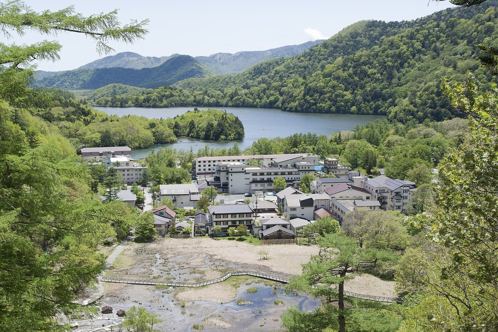 緑の山に囲まれた湯ノ湖と、手前の湯元温泉の宿の建物と湿原の木道